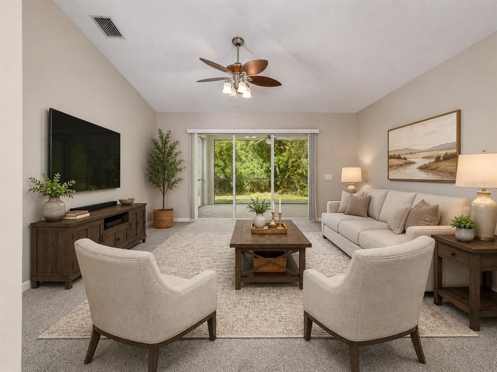 A living room features a vaulted ceiling, neutral furniture, a coffee table, and sliding glass doors — 25342 LEXINGTON OAKS BOULEVARD, WESLEY CHAPEL, FL
