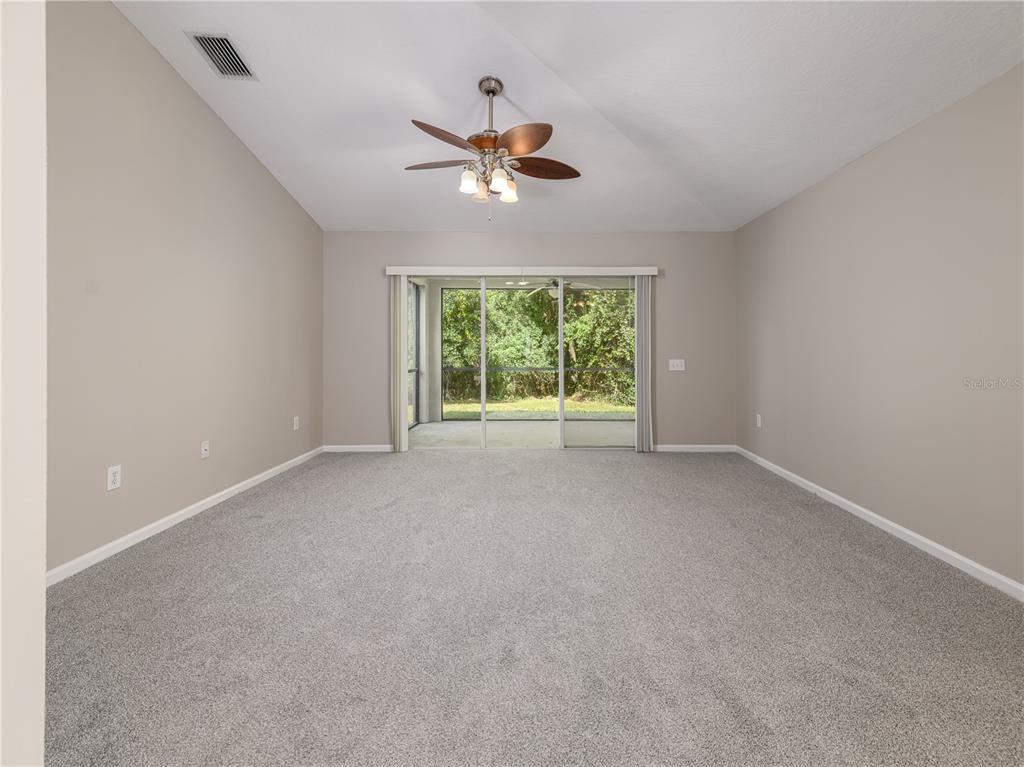 A spacious living room features gray carpeting, neutral walls, a ceiling fan, and sliding glass doors — 25342 LEXINGTON OAKS BOULEVARD, WESLEY CHAPEL, FL