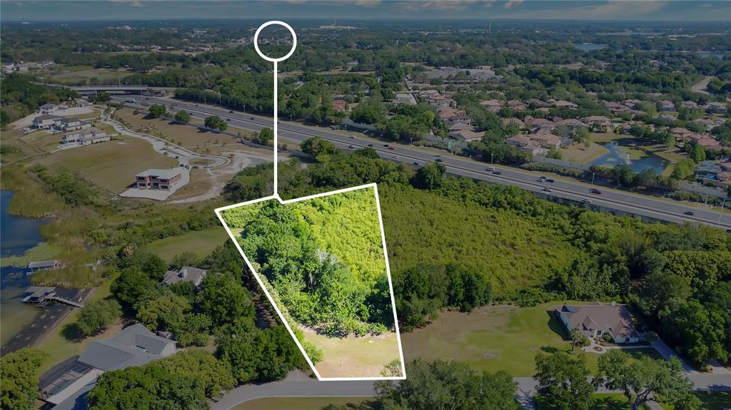 An aerial view shows a vacant, wooded lot outlined in white near a highway — 1661 ROBERTS LANDING ROAD, WINDERMERE, FL