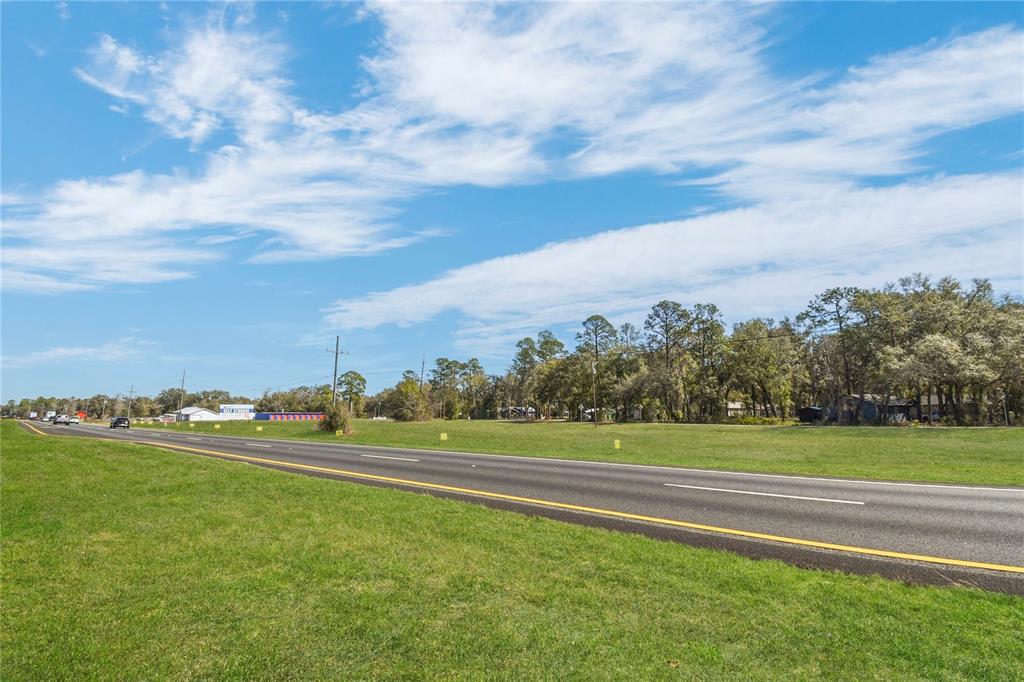 A paved road runs alongside a large, grassy vacant lot with trees in the background — 9150 SE COUNTY ROAD 221, HAMPTON, FL