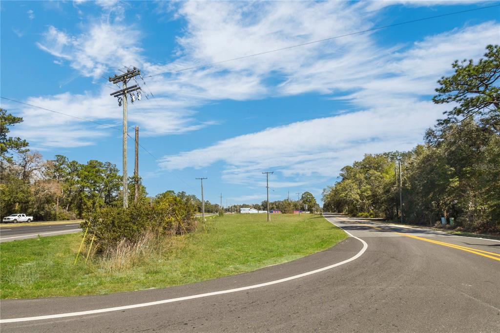 A paved road curves past a grassy lot with utility poles under a blue sky — 9150 SE COUNTY ROAD 221, HAMPTON, FL