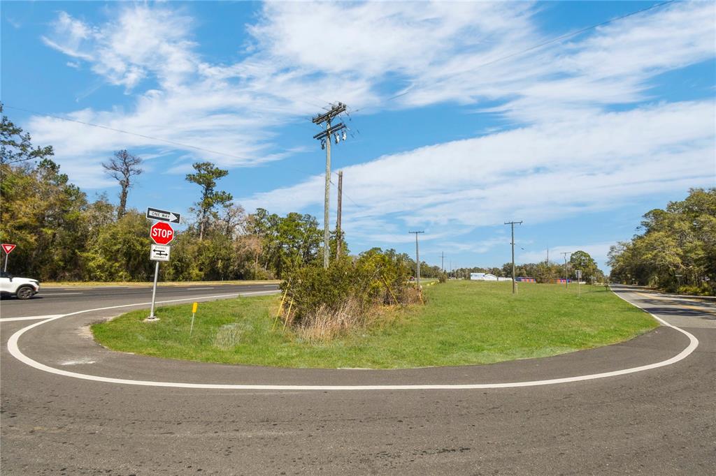 A paved road curves around a grassy median featuring a stop sign and utility pole — 9150 SE COUNTY ROAD 221, HAMPTON, FL