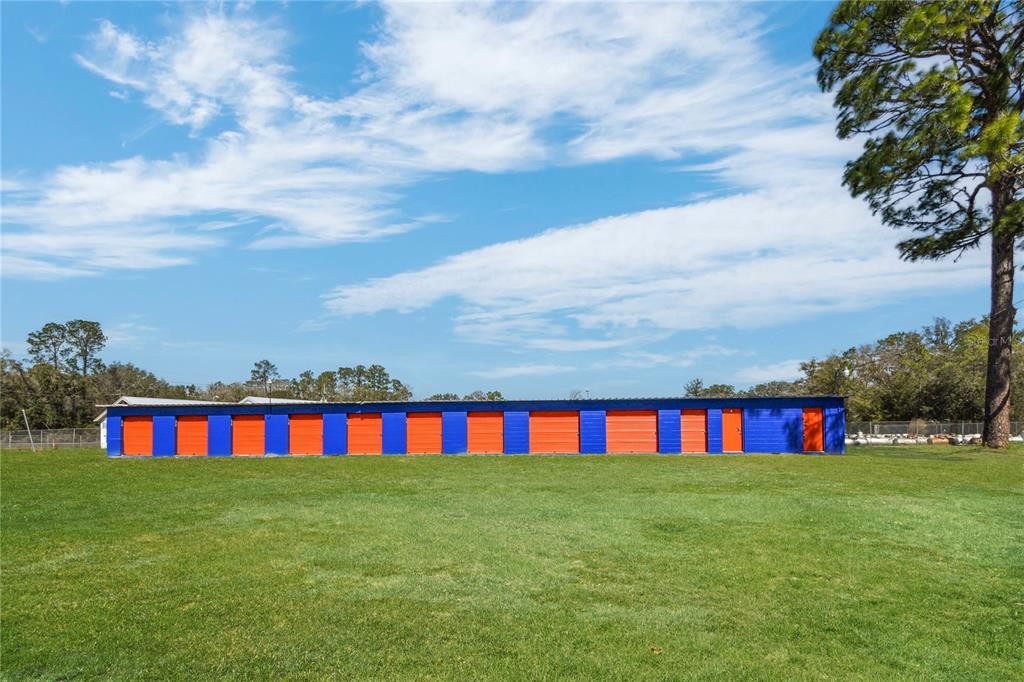 A long, single-story storage unit building with alternating blue and orange doors sits on grass — 9150 SE COUNTY ROAD 221, HAMPTON, FL