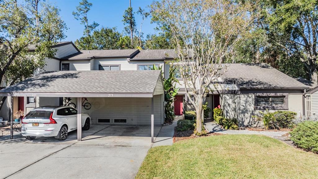 A two-story townhouse exterior features a covered carport with a white SUV parked inside — 215 WOODS LANDING TRAIL, OLDSMAR, FL