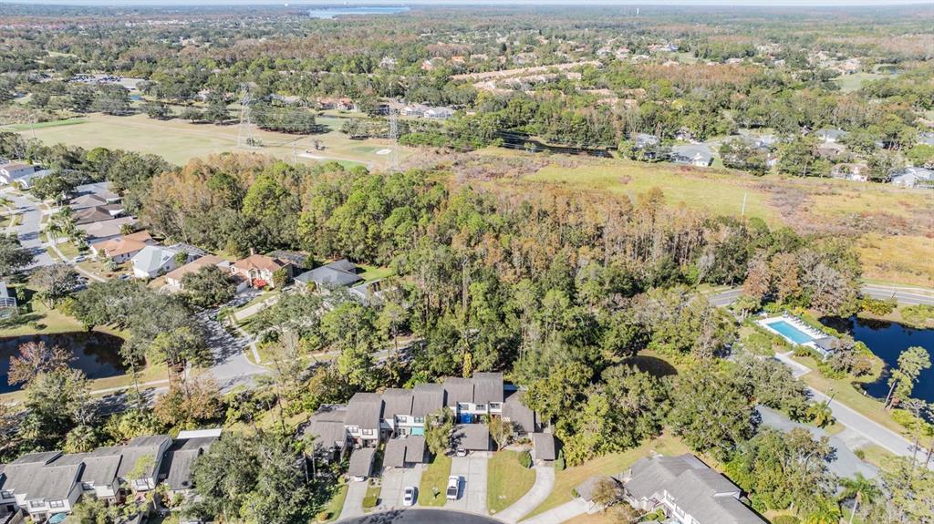 An aerial view shows a suburban neighborhood with townhomes, wooded areas, and a swimming pool — 215 WOODS LANDING TRAIL, OLDSMAR, FL