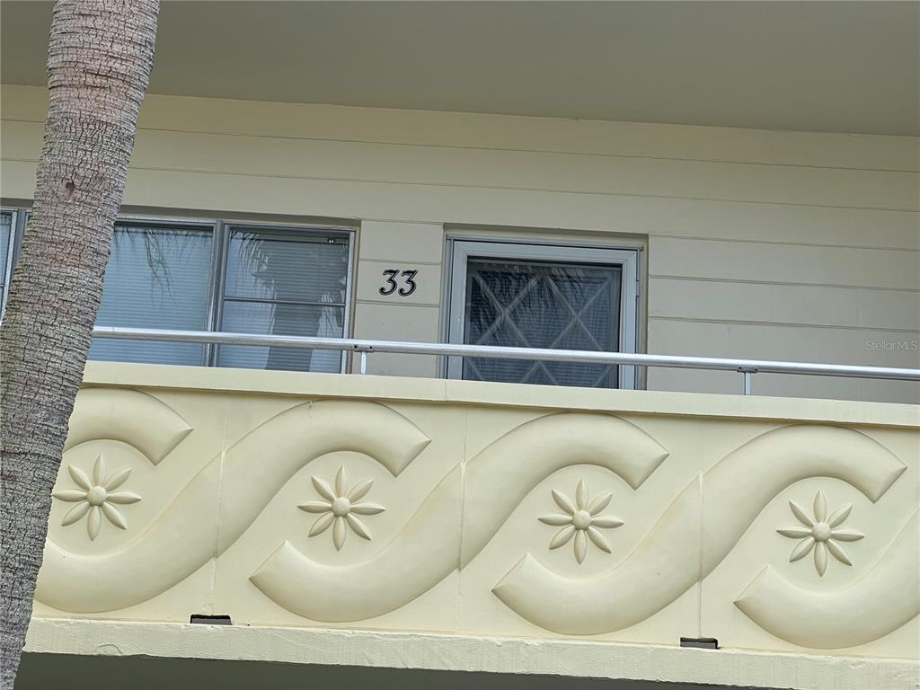 A balcony with a decorative railing featuring wave patterns and star motifs sits outside unit 33 — 2361 ECUADORIAN WAY UNIT 33, CLEARWATER, FL