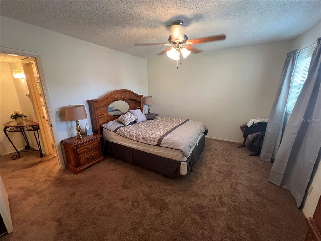 A bedroom features brown carpeting, a wooden headboard, a ceiling fan, and a doorway — 2361 ECUADORIAN WAY UNIT 33, CLEARWATER, FL