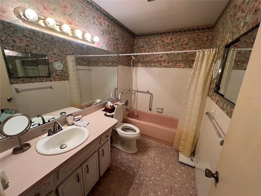 A bathroom features a pink bathtub, a vanity with a pink countertop, and floral wallpaper — 2361 ECUADORIAN WAY UNIT 33, CLEARWATER, FL