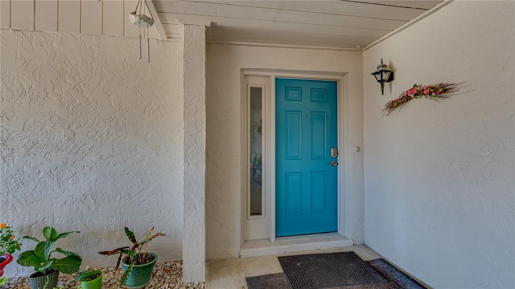 A bright blue front door with a side light sits under a covered entryway — 1219 16TH CIRCLE SE UNIT 1219, LARGO, FL