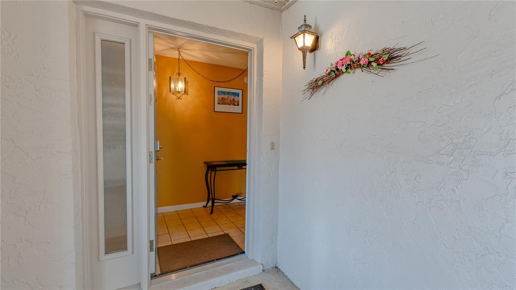 A view from a covered porch looking into an entryway with tiled floors and yellow walls — 1219 16TH CIRCLE SE UNIT 1219, LARGO, FL