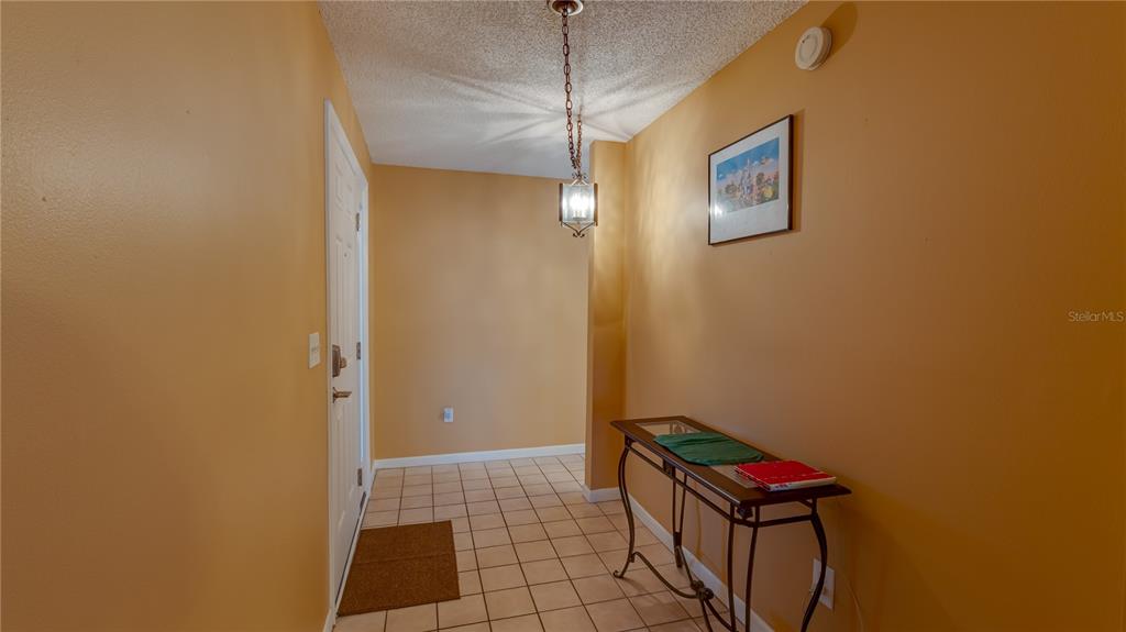 An entryway features tan walls, a tiled floor, a hanging pendant light, and a console table — 1219 16TH CIRCLE SE UNIT 1219, LARGO, FL