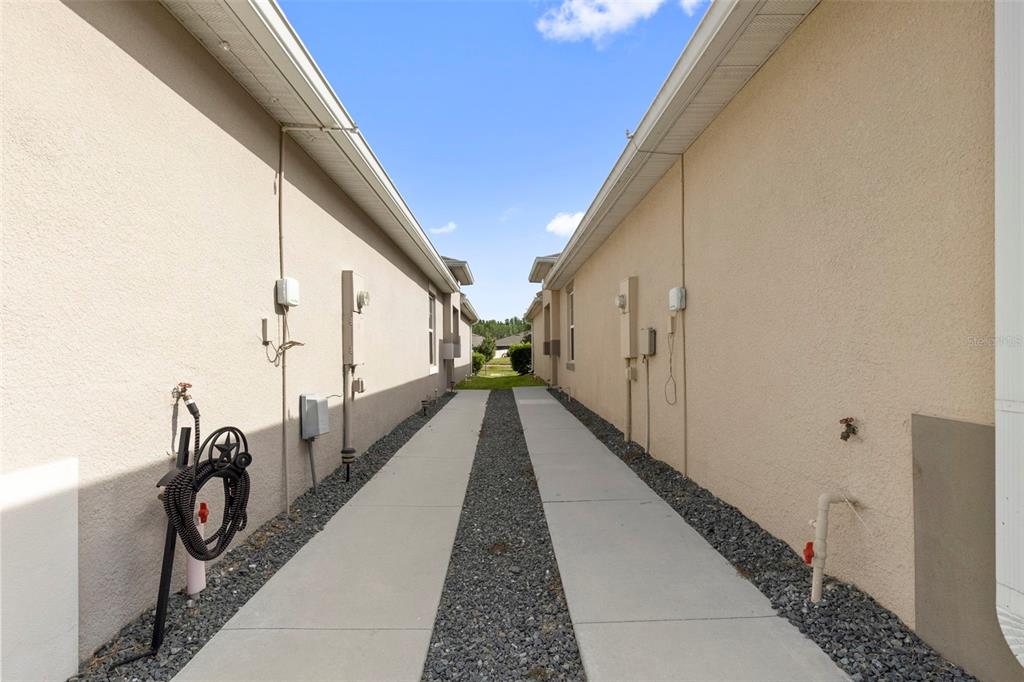 A narrow outdoor walkway between two beige stucco houses features concrete paths and gravel — 17784 TURNING LEAF CIRCLE, LAND O LAKES, FL
