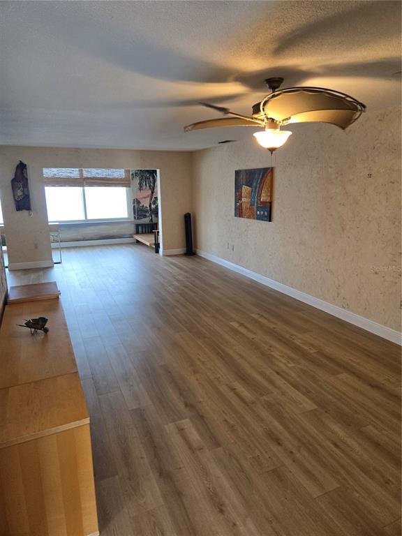 A living room with light wood-look flooring, textured walls, and a ceiling fan — 7 DUNOON PLACE UNIT 309, DUNEDIN, FL