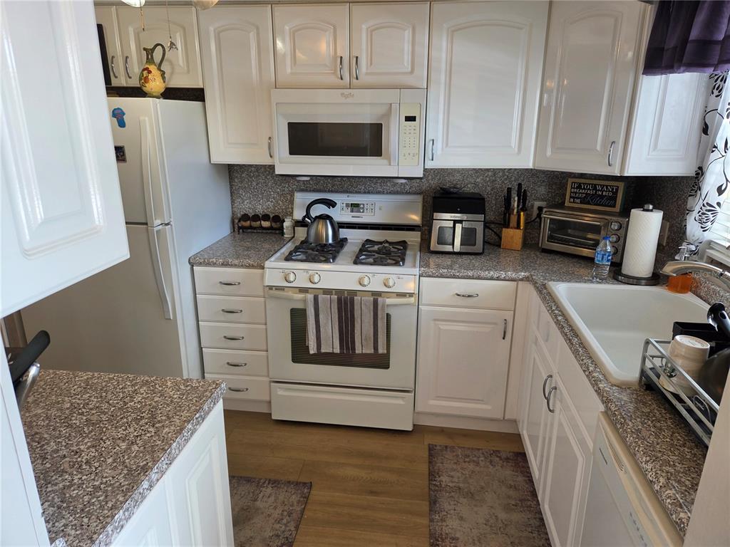 A kitchen with white cabinets, granite countertops, a gas stove, and a white refrigerator — 7 DUNOON PLACE UNIT 309, DUNEDIN, FL