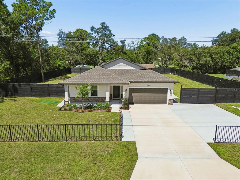 A single-story house with a covered front porch, a dark garage, and a landscaped yard — 12326 DEEP CREEK DRIVE, SPRING HILL, FL