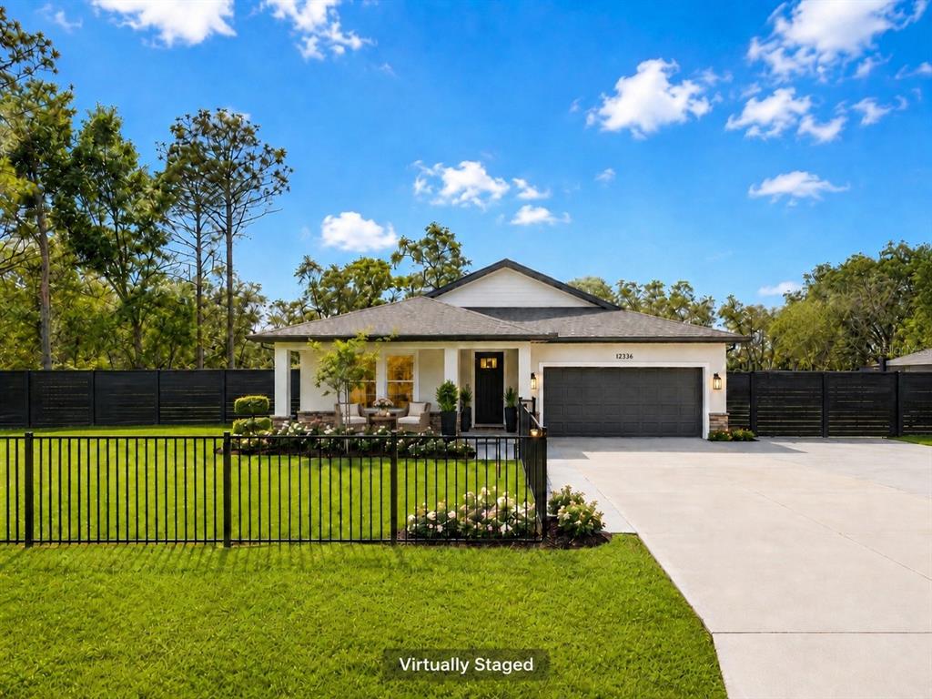 A covered porch features two wicker chairs, a small table, and a dark front door — 12326 DEEP CREEK DRIVE, SPRING HILL, FL