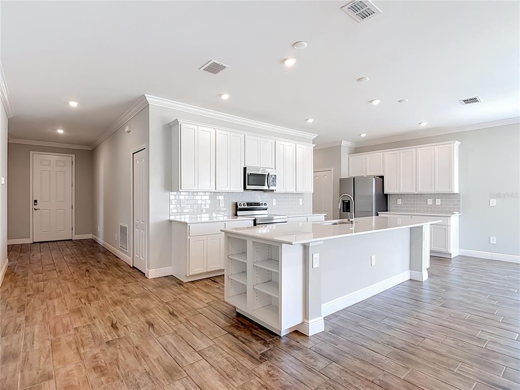 A kitchen features white cabinets, a central island with shelving, and wood-look tile flooring — 8792 CASCADE PRICE CIRCLE, NORTH FORT MYERS, FL