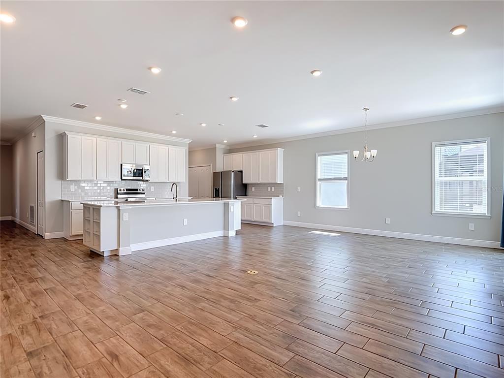 A kitchen with white cabinets and a large island opens into a spacious living area — 8792 CASCADE PRICE CIRCLE, NORTH FORT MYERS, FL
