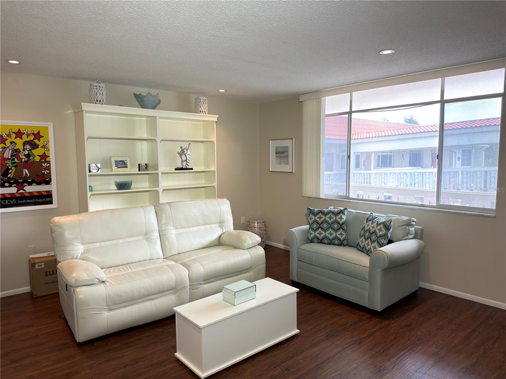 A living room features a white sofa, a matching loveseat, a coffee table, and bookshelves — 2650 PEARCE DRIVE UNIT 409, CLEARWATER, FL