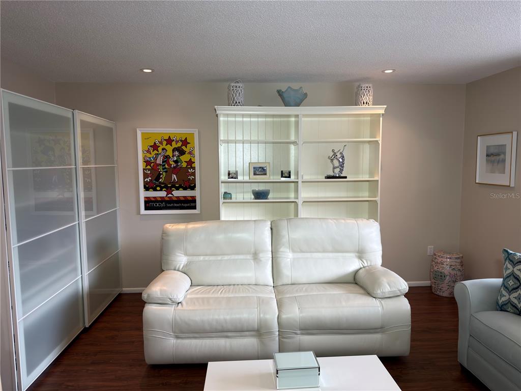 A living room features a white leather sofa, a large bookcase, and a framed poster — 2650 PEARCE DRIVE UNIT 409, CLEARWATER, FL