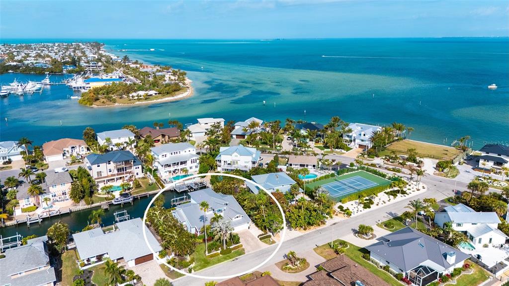 An aerial view shows a coastal neighborhood with a circled house and a tennis court — 605 N POINT DRIVE, HOLMES BEACH, FL