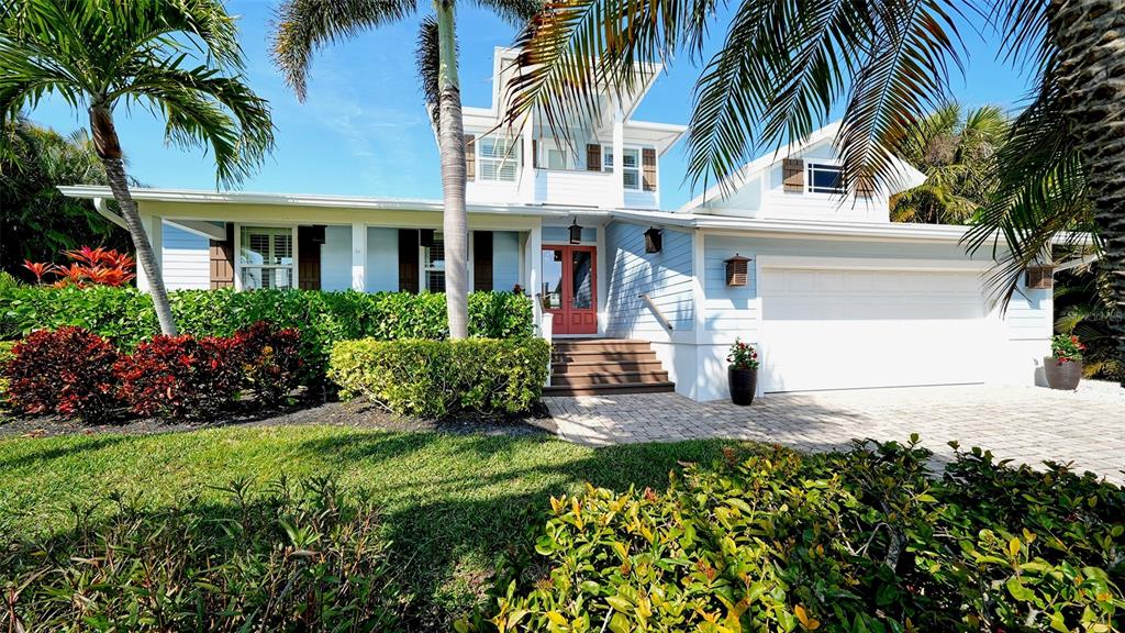 A light blue two-story house features a white garage, red front door, and palm trees — 605 N POINT DRIVE, HOLMES BEACH, FL