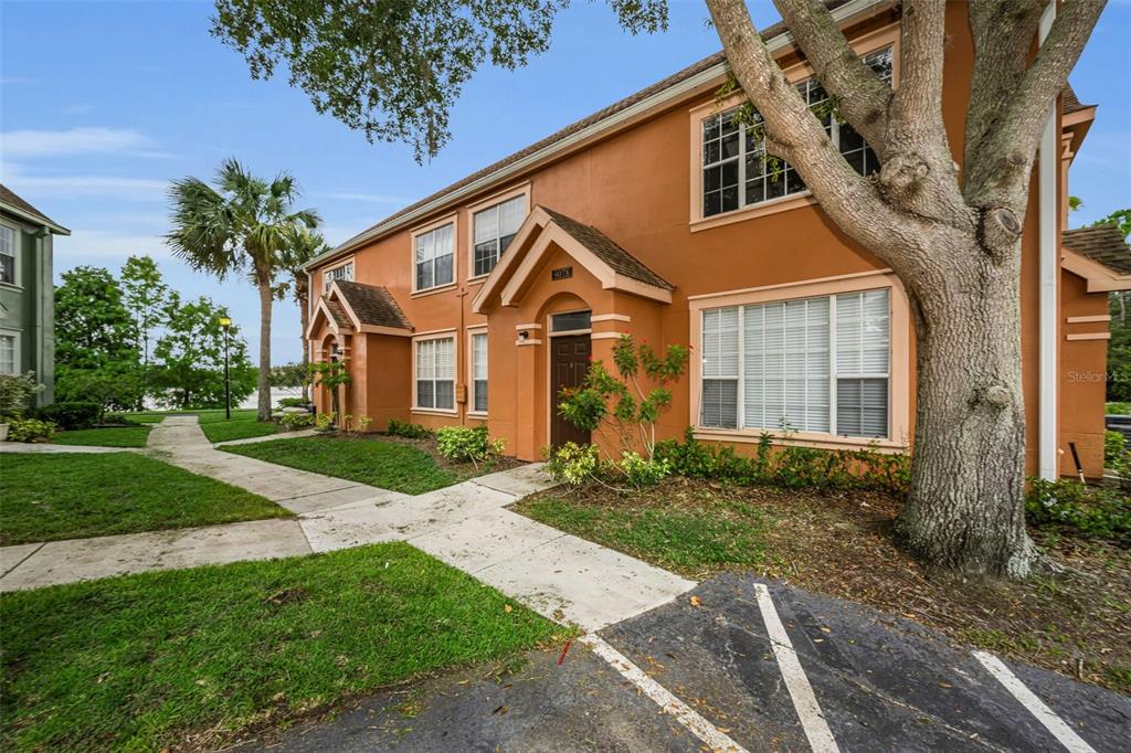 An exterior view of a two-story orange stucco apartment building with a sidewalk and tree — 9078 LAKE CHASE ISLAND WAY UNIT 9078, TAMPA, FL