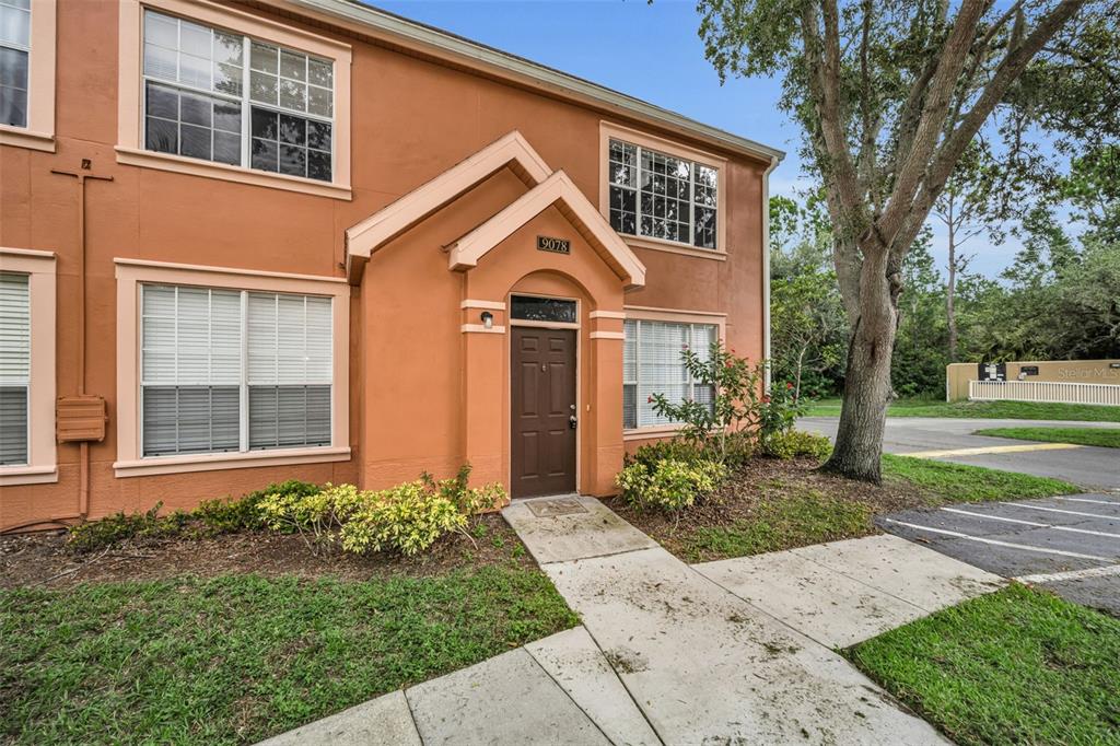 An exterior view of a two-story orange stucco townhouse with a brown front door — 9078 LAKE CHASE ISLAND WAY UNIT 9078, TAMPA, FL
