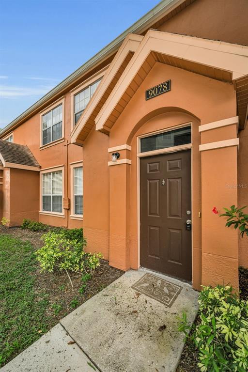 The exterior of a two-story orange stucco building features a brown front door and windows — 9078 LAKE CHASE ISLAND WAY UNIT 9078, TAMPA, FL