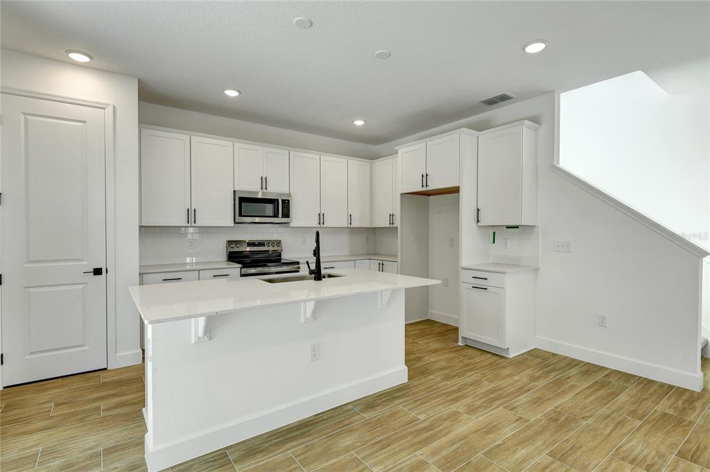 A modern kitchen features white cabinetry, a central island, stainless steel appliances, and wood-look flooring — 1010 CLOUD RIDGE COURT, MOUNT DORA, FL