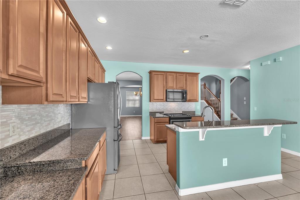 A kitchen features light wood cabinets, granite countertops, a stainless steel refrigerator, and teal walls — 10626 LIBERTY BELL DRIVE, TAMPA, FL