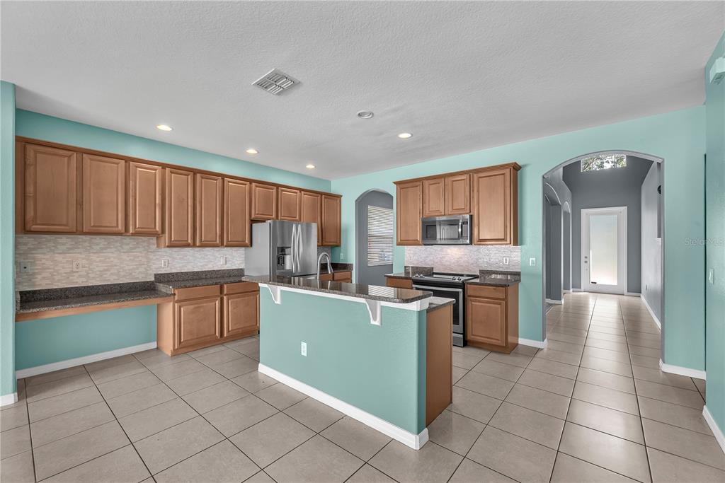 A kitchen with light blue walls, wood cabinets, granite countertops, and tile flooring — 10626 LIBERTY BELL DRIVE, TAMPA, FL