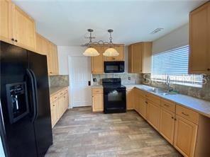 A kitchen features light wood cabinets, black appliances, and a light-colored tile floor — 1409 MADRID WAY, WINTER SPRINGS, FL