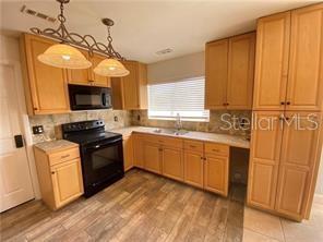 A kitchen features light wood cabinets, black appliances, a double pendant light, and wood-look flooring — 1409 MADRID WAY, WINTER SPRINGS, FL