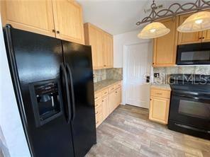 A kitchen features light wood cabinets, black appliances, and wood-look tile flooring — 1409 MADRID WAY, WINTER SPRINGS, FL