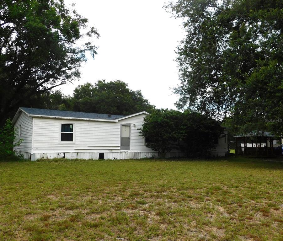 A single-story white mobile home sits on a grassy lot surrounded by large trees — 30501 CLEARVIEW DRIVE, WESLEY CHAPEL, FL