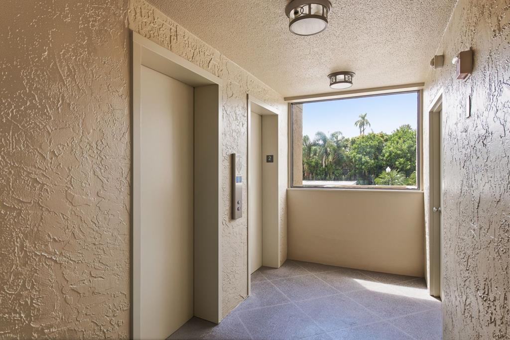 An elevator lobby with textured walls, tile flooring, and a window overlooking trees — 2621 COVE CAY DRIVE UNIT 203, CLEARWATER, FL