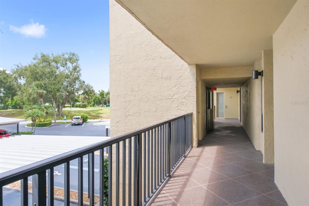 An outdoor apartment walkway with a metal railing overlooks a parking lot and trees — 2621 COVE CAY DRIVE UNIT 203, CLEARWATER, FL