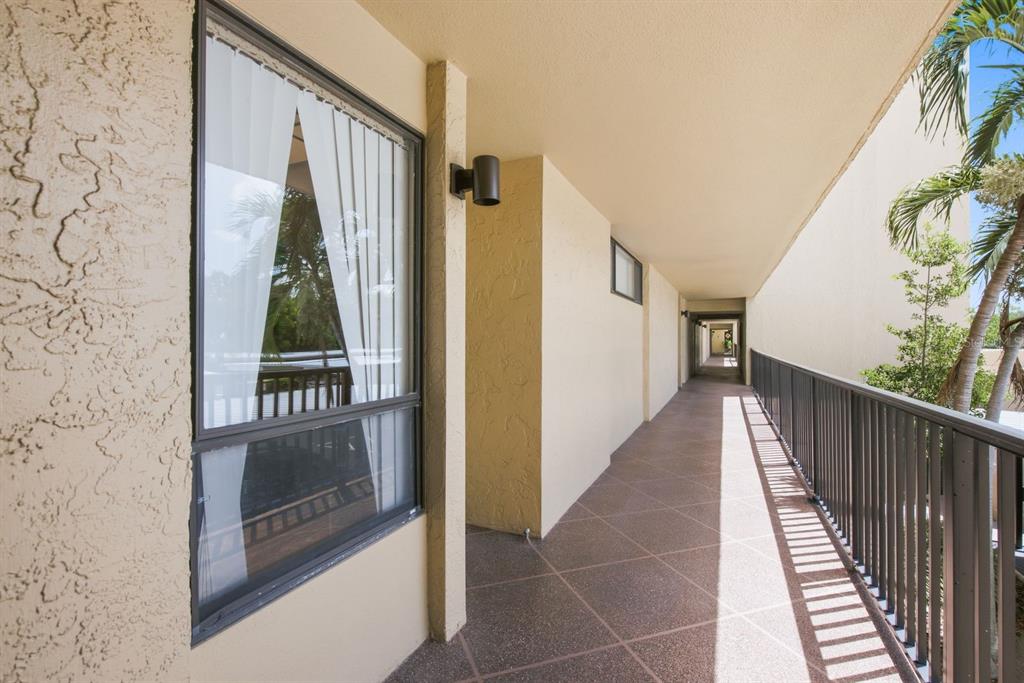 An outdoor walkway with a metal railing, textured walls, and a window with white curtains — 2621 COVE CAY DRIVE UNIT 203, CLEARWATER, FL