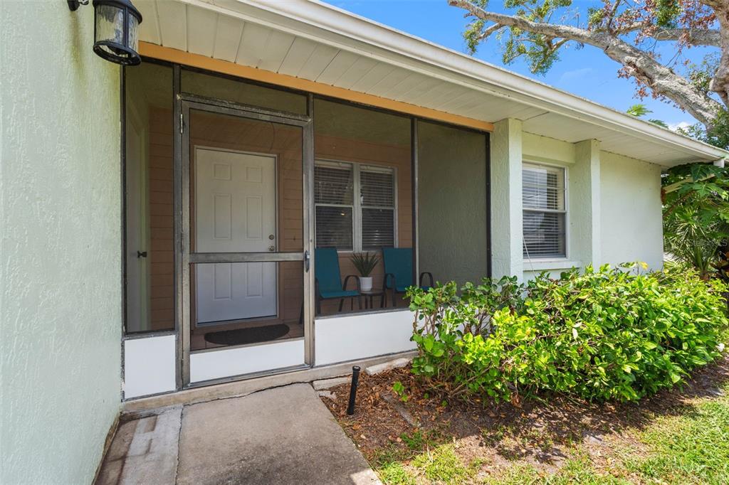 A screened-in front porch with a white door, two chairs, and adjacent landscaping — 2833 ORANGE TREE CIRCLE N UNIT A, PALM HARBOR, FL