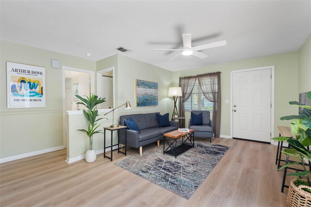 A living room features light green walls, wood-look flooring, a grey sofa, and a ceiling fan — 2833 ORANGE TREE CIRCLE N UNIT A, PALM HARBOR, FL