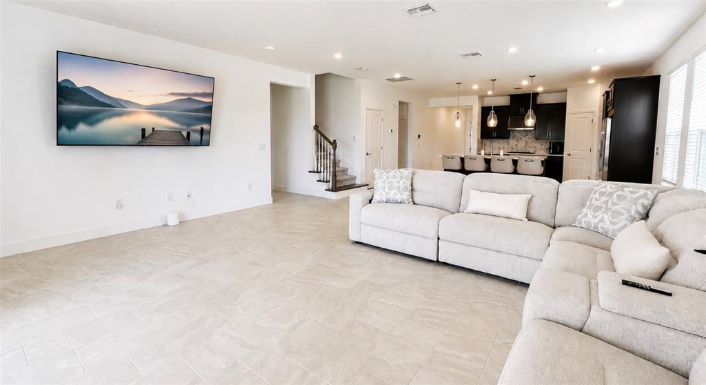 A living room with light tile flooring, a large sectional sofa, and an open kitchen — 1854 LONGLINER LOOP, WESLEY CHAPEL, FL