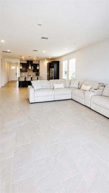 A spacious open-concept living room features light tile flooring and a large sectional sofa — 1854 LONGLINER LOOP, WESLEY CHAPEL, FL