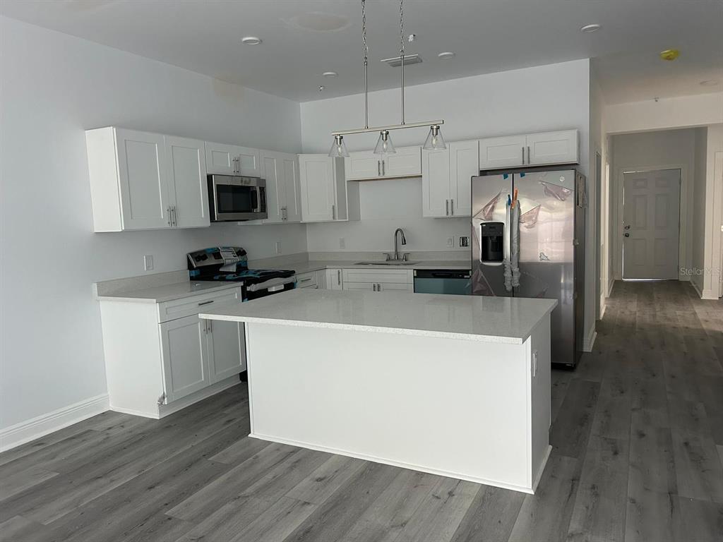 A modern kitchen features white cabinets, stainless steel appliances, a center island, and gray flooring — 705 S ORANGE AVENUE, BARTOW, FL