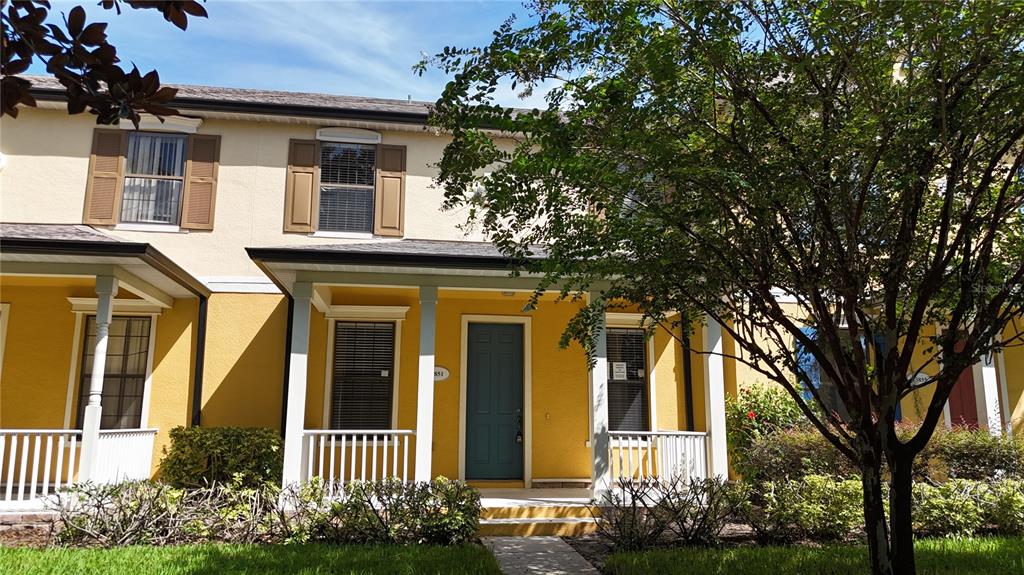 A two-story yellow townhouse with a front porch, white railings, and a dark door — 13851 BEAUREGARD PLACE, ORLANDO, FL