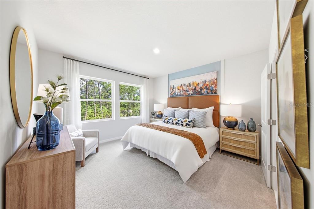 A bedroom features a king bed, a blue accent wall, and a view of trees — 1132 WILD CREST LANE, DAYTONA BEACH, FL