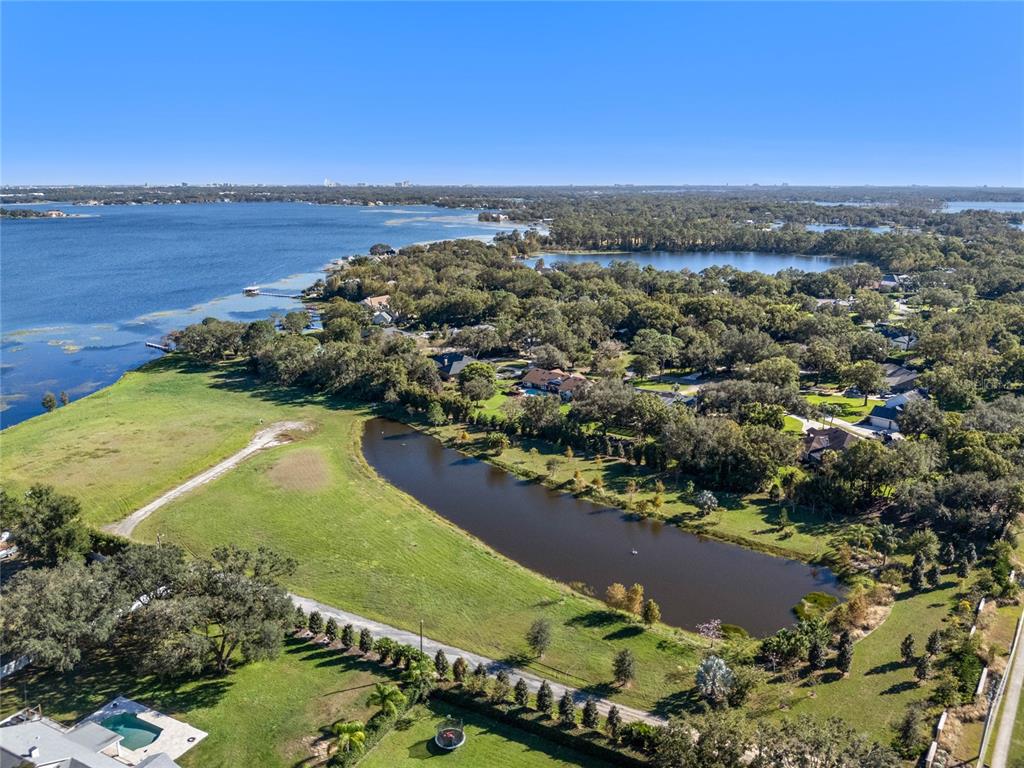 An aerial view shows a pond, grassy fields, and houses surrounded by trees near water — 10948 DOWN PARK LANE, WINDERMERE, FL