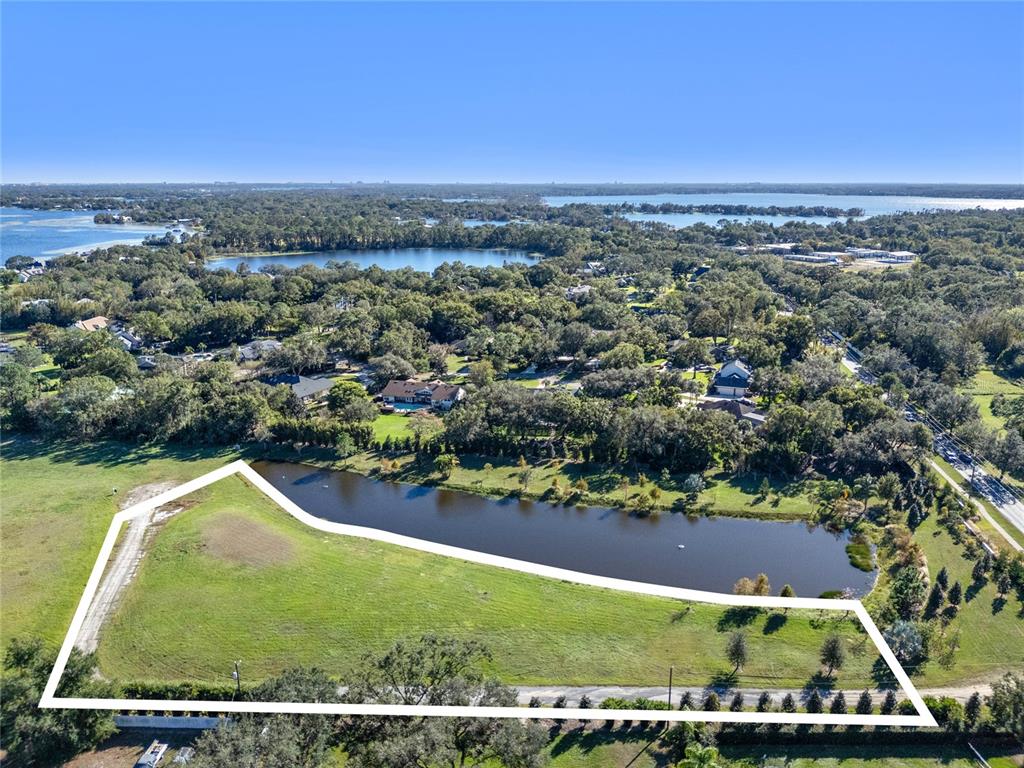 An aerial view shows a grassy plot of land bordering a pond and wooded area — 10948 DOWN PARK LANE, WINDERMERE, FL