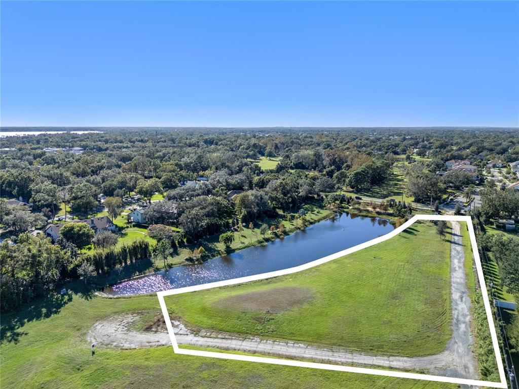 An aerial view shows a vacant, grassy lot bordering a pond with a dirt driveway — 10948 DOWN PARK LANE, WINDERMERE, FL