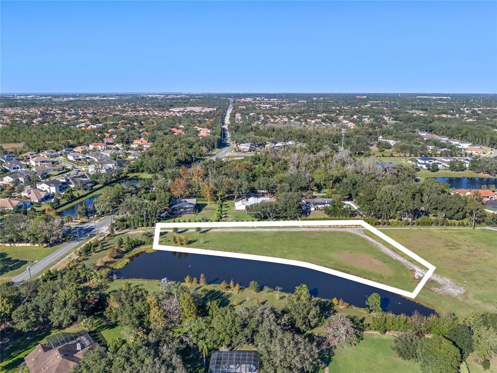 An aerial view shows a vacant, grassy lot bordered by a pond and residential homes — 10948 DOWN PARK LANE, WINDERMERE, FL